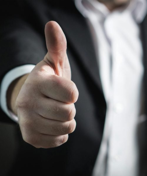 A close-up of a man's thumbs up gesture, symbolizing success and agreement.